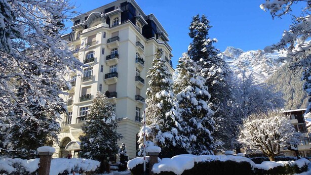 A multi-story hotel with balconies, surrounded by snow-covered trees and mountains in the background. - Bright apartment for 5, Chamonix center, parking included (Chamonix-Mont-Blanc)