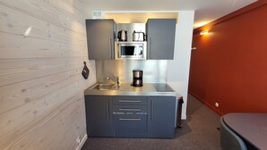 Una cocina compacta con gabinetes grises, un lavamanos de acero inoxidable y un microondas.