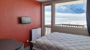 Una habitación de hotel con cama, televisión y ventana que da a un paisaje nevado.