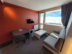 Une chambre d’hôtel compacte comprenant un canapé, une petite table, un téléviseur et une fenêtre donnant sur un paysage enneigé.