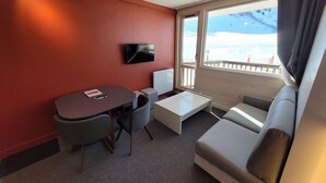 Habitación de hotel compacta con sofá, una mesita, televisor y ventana con vistas a un paisaje nevado.