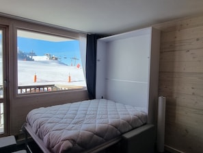 Ein Zimmer mit einem Bett, einem Fenster mit Blick auf eine verschneite Landschaft und Holzverkleidung an der Wand.