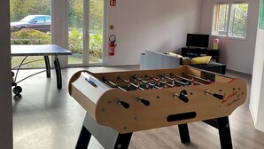 Une pièce avec un baby-foot, une télévision et une fenêtre donnant sur une voiture et sur la verdure à l’extérieur.