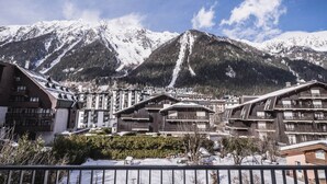 A mountain resort with chalet-style buildings, snow-covered mountains, and a clear sky. - 3-star duplex for 6 pers, Chamonix, private parking (Chamonix-Mont-Blanc)