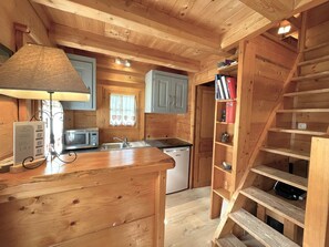 A wooden cabin interior with a kitchen area, a microwave, a sink, and a staircase.