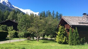 Una cabana de fusta amb un teulat inclinat, envoltada d'un jardí ben cuidat i una vista despejada d'una muntanya nevada al fons.