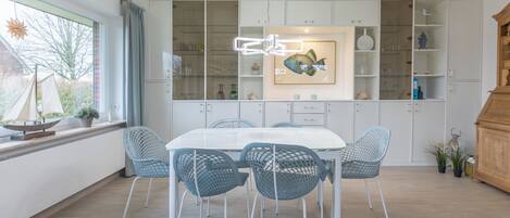 Un espace repas moderne avec une table blanche et des chaises bleues, un tableau décoratif représentant des poissons et un buffet en bois.