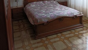 A bedroom with a wooden bed, a nightstand with a lamp, a chandelier, and a window with curtains.