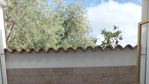 A patio with a white table and four white plastic chairs, a stone wall, and a tiled roof.