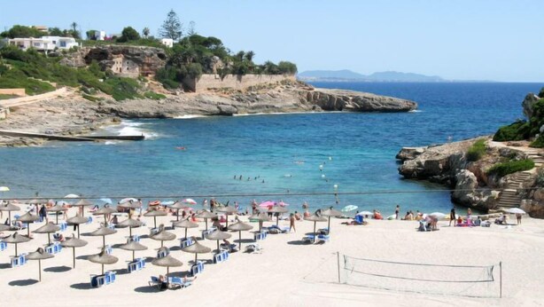 A beach with umbrellas and lounge chairs, rocky cliffs, and a clear view of the sea. - Murada Lisboa by Interhome (Cala Murada)