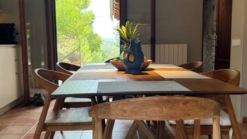 Un comedor con una mesa y sillas de madera, una lámpara colgante y vistas al exterior con vegetación.