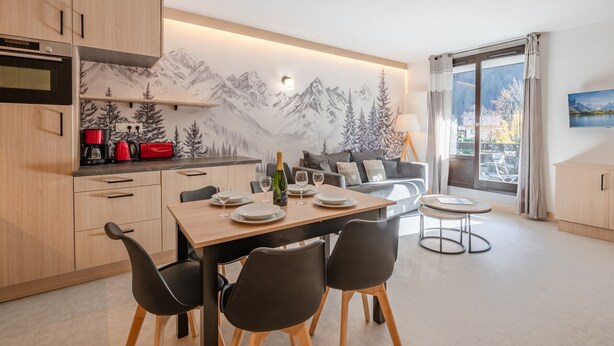 A modern kitchen with wooden cabinets, a dining area with a table set for four, and a cozy seating area with a sofa and chairs.