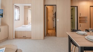 A modern hotel room with a bed, a dining table with plates and glasses, and built-in wooden cabinets.