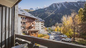 A balcony with a view of a mountain range, a parking area, and a building with multiple floors and balconies.