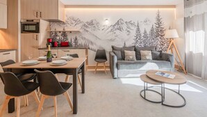 A modern apartment with a kitchen, dining area, and living room. It features a mountain mural, a sofa, a coffee table, and a lamp.
