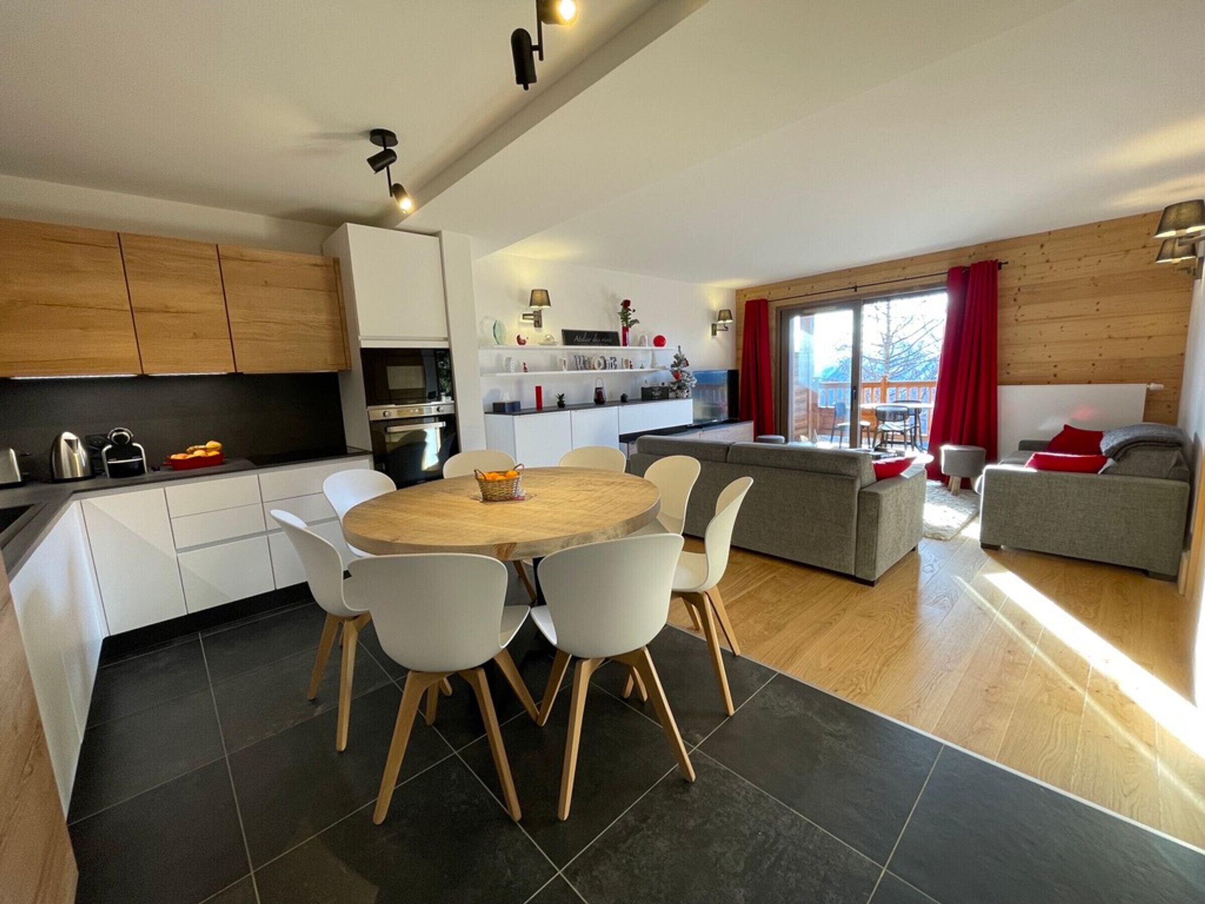 A modern kitchen with white cabinets, a dining area with a round table and chairs, and a living area with a sofa and a window.