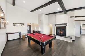 A pool table in a room with a fireplace, wooden floors, and a modern design.