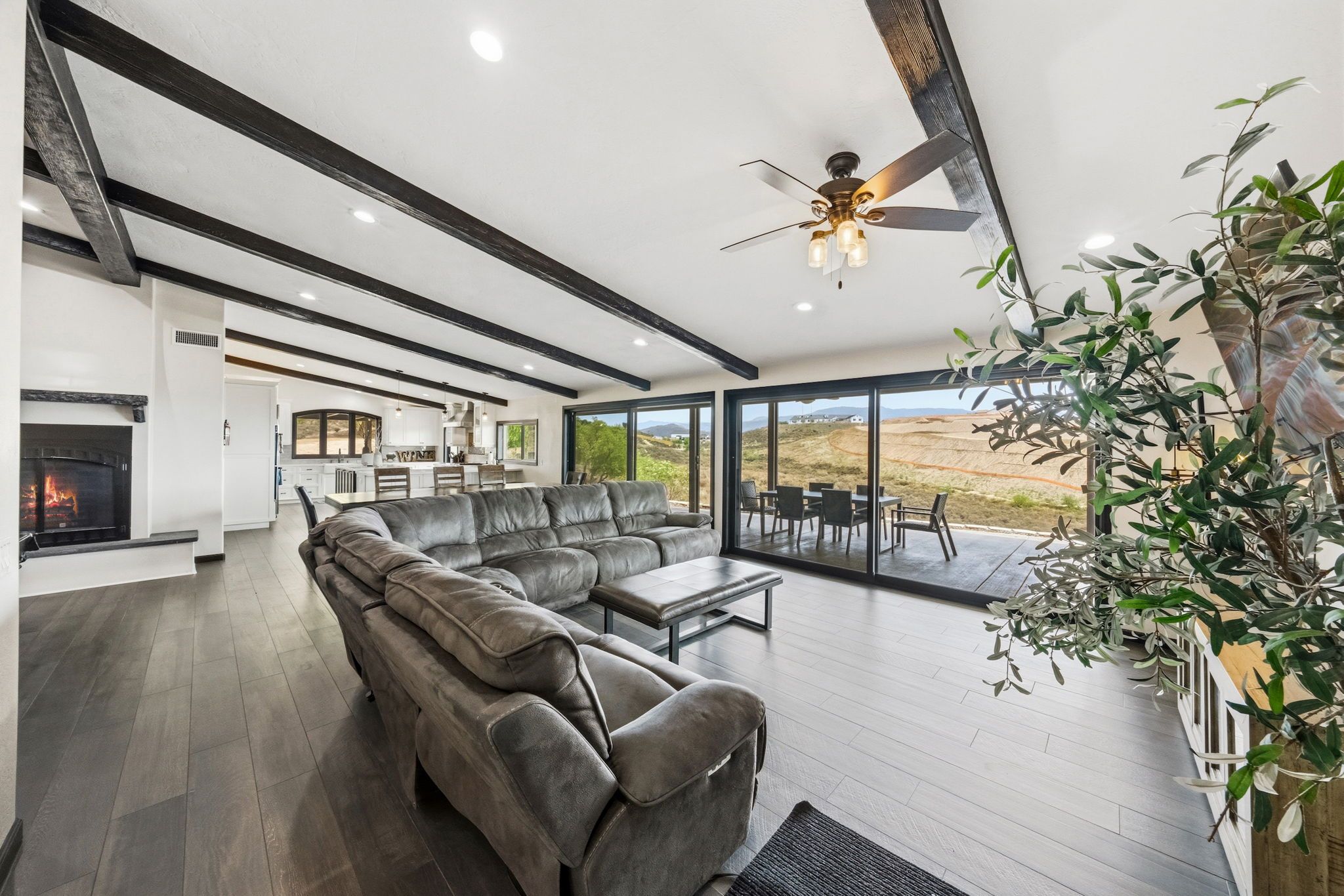 A spacious living room with a fireplace, a large sectional sofa, and a dining area with a view of the landscape.