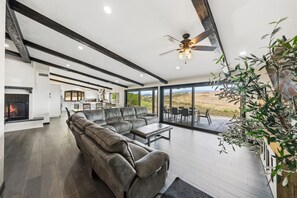 A spacious living room with a fireplace, a large sectional sofa, and a dining area with a view of the landscape. - Five bedroom hilltop view home with spa and fire pits (Temecula)
