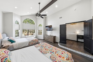 A bedroom with two beds, a ceiling fan, a TV, a dresser, and a door leading to a bathroom.