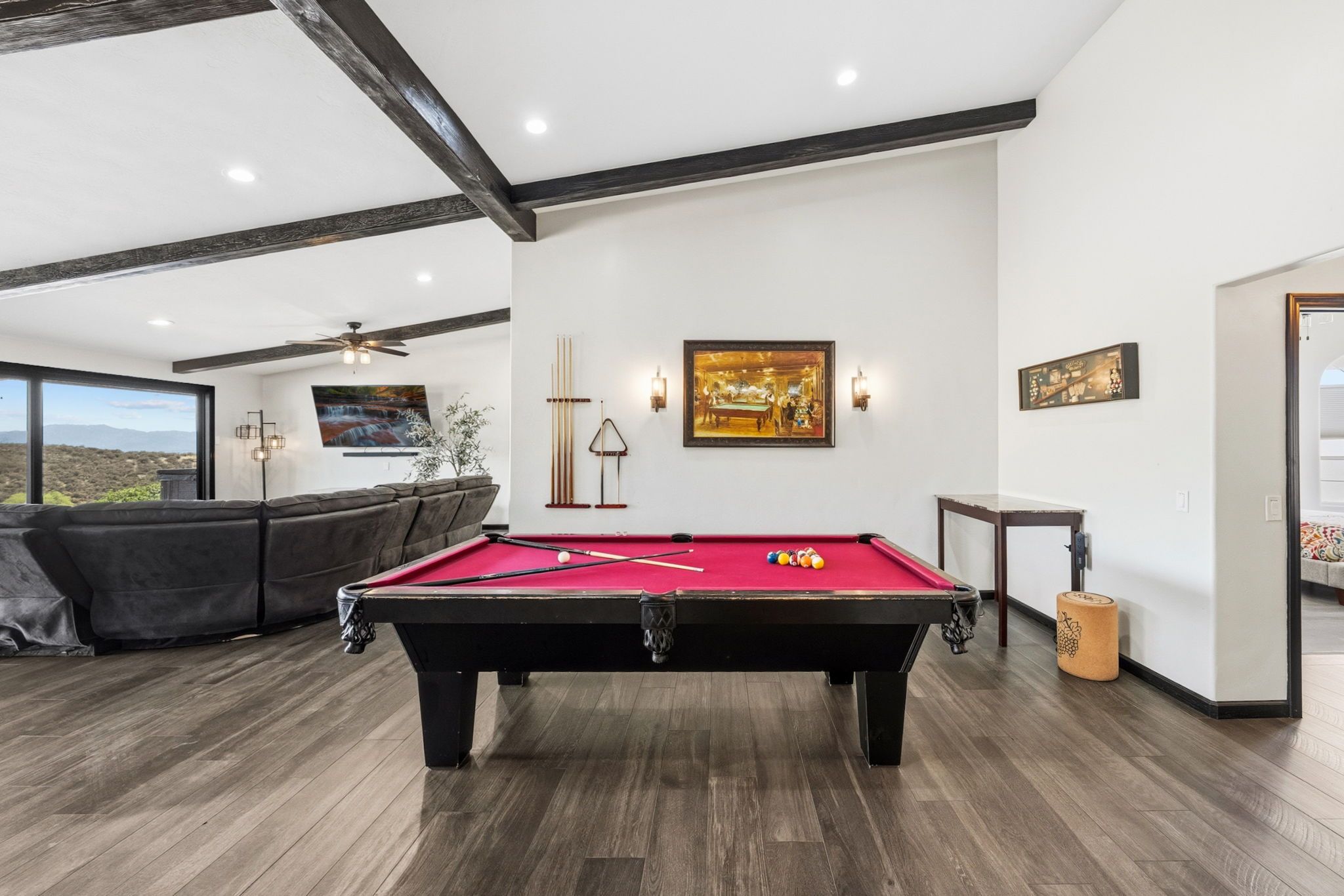 Une table de billard dans une pièce dotée d’un plancher en bois, d’un canapé et d’une grande fenêtre.