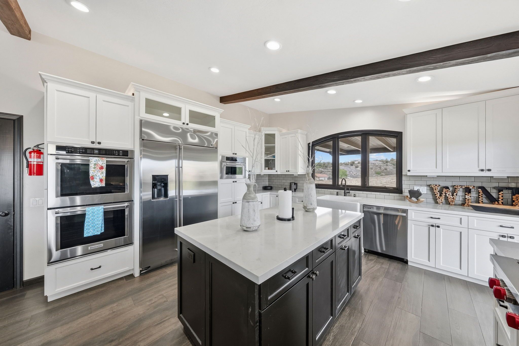 Uma cozinha moderna com armários brancos, eletrodomésticos de aço inoxidável, uma ilha central e uma grande janela com vista.