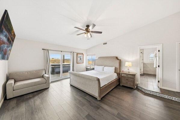 A bedroom with a bed, a sofa, a nightstand, a ceiling fan, and a view through a window.