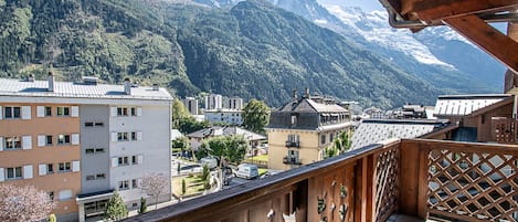 A balcony with a wooden railing overlooking a town with buildings and snow-capped mountains in the background.