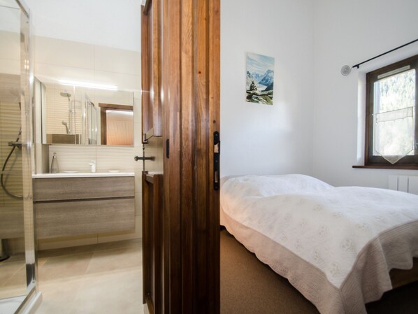 A bedroom with a bed, a window with a view, a bathroom with a shower, and a painting on the wall. - Charming 4 pers apartment with parking and balcony in Chamonix (Chamonix-Mont-Blanc)