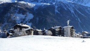 Un complejo turístico en la montaña cubierto de nieve, con edificios de estilo chalete, una pista de esquí y un cielo azul despejado.