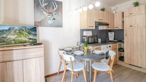 A modern kitchen with wooden cabinets, a dining table with chairs, a painting of a deer, and a mountain landscape on the wall. - Charming studio with Mont-Blanc view, Wifi and pets allowed (Chamonix-Mont-Blanc)
