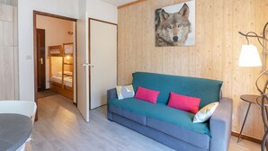 A modern room with a grey sofa, teal cushions, and a wooden wall with a wolf painting. - Charming studio with Mont-Blanc view, Wifi and pets allowed (Chamonix-Mont-Blanc)