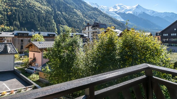 A mountain town with traditional buildings, a wooden balcony, and snow-capped mountains in the background. - Charming studio with Mont-Blanc view, Wifi and pets allowed (Chamonix-Mont-Blanc)