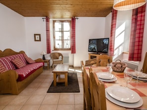 Un salon chaleureux avec un canapé, une table basse en bois, un téléviseur et une table à manger dressée pour deux personnes.