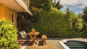 Un patio con piscina, rodeado por un muro de piedra y abundante vegetación.