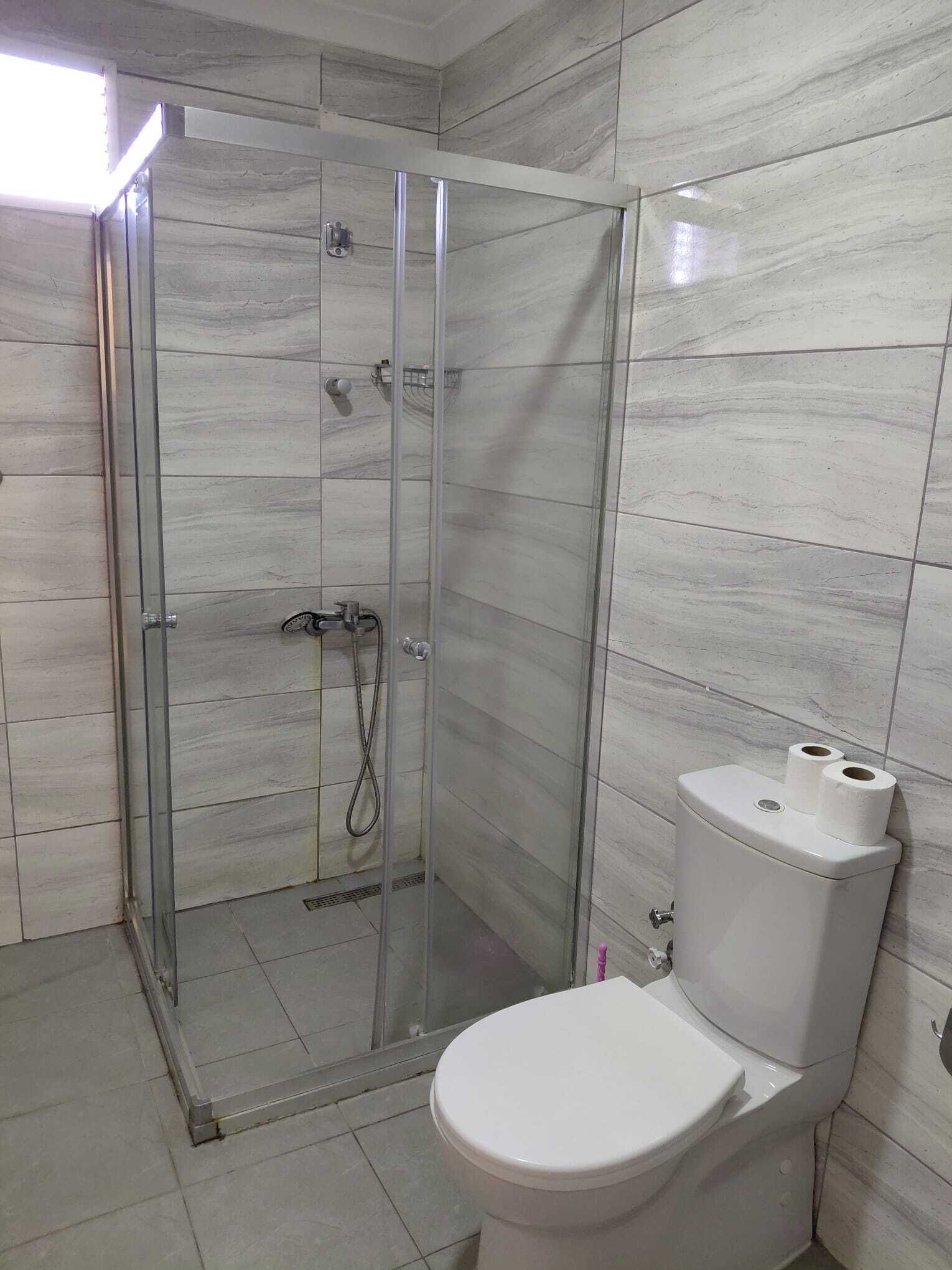 Ein Badezimmer mit einer Duschkabine, einer Toilette und Fliesenwänden.