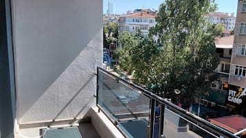 A balcony with a glass railing, a red awning, and a view of the cityscape.