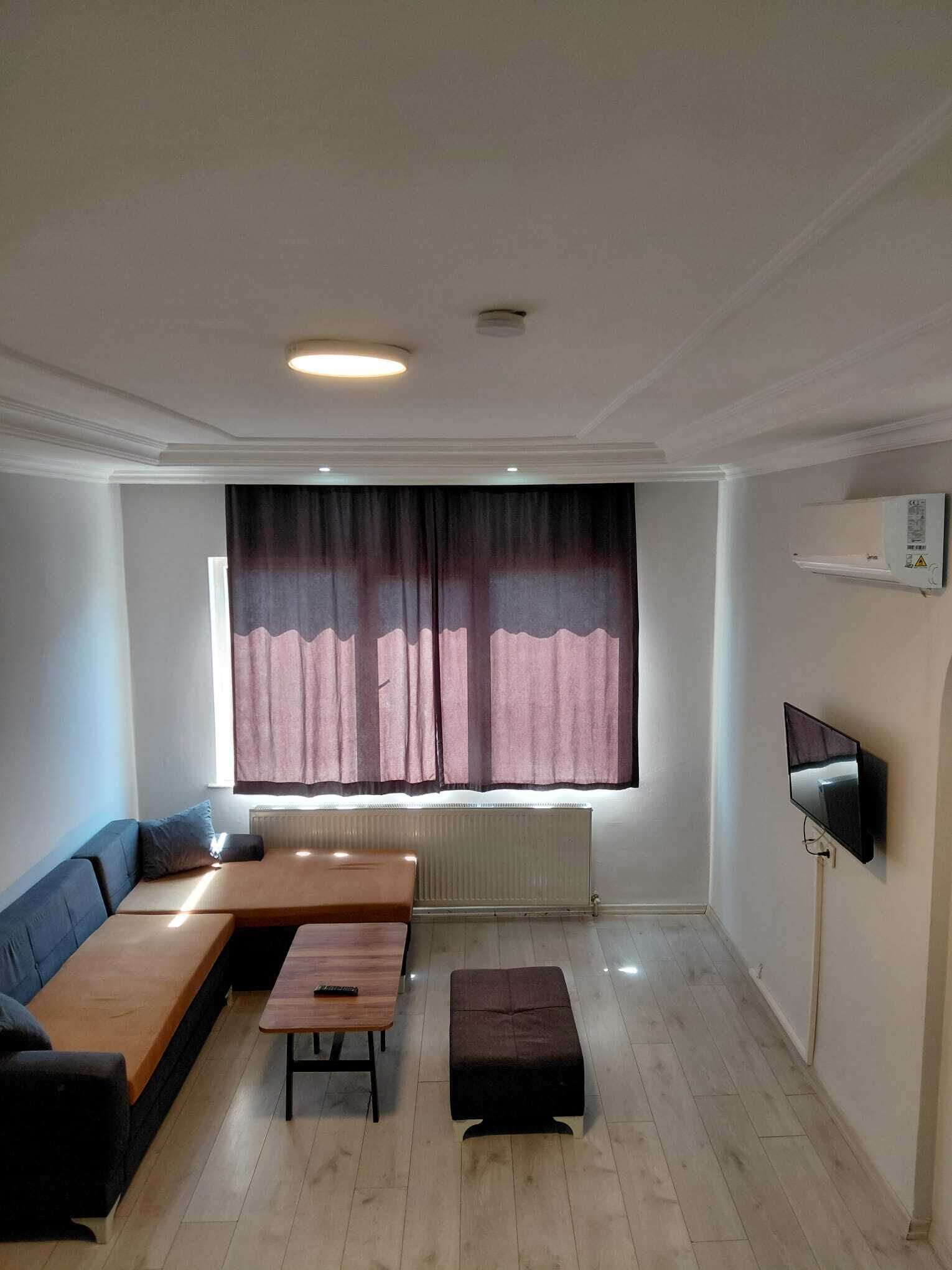 Una sala de estar con un sofá, una mesa de centro, un televisor y una ventana con cortinas.