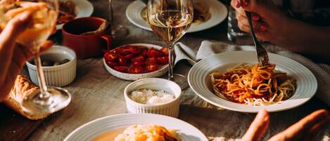 A dining table with plates of food, glasses of wine, and a person using a fork.