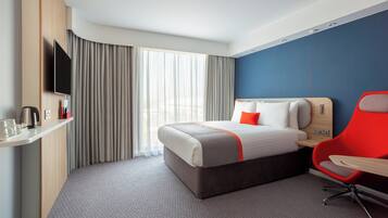 Una habitación de hotel con una cama, una silla roja, un televisor y un escritorio con una tetera.