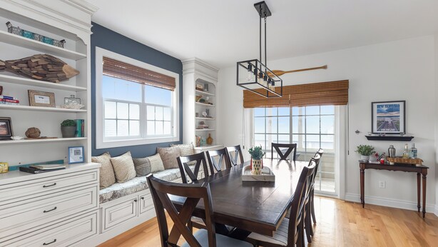 Un comedor con una mesa y sillas de madera, rodeado de muebles de cocina blancos con estanterías y un banco empotrado.