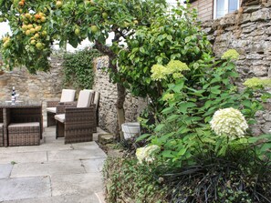 Une terrasse dotée de meubles en osier, d’un mur en pierre et d’un arbre aux feuilles vertes et aux fruits jaunes.