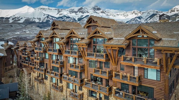 A multi-story lodge with wooden balconies and large windows, set against a backdrop of snow-capped mountains.