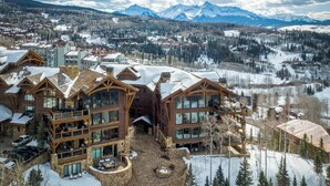 A large lodge with multiple floors, a stone courtyard, and a view of snow-covered mountains.