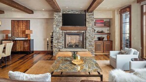 A living room with a stone fireplace, wooden beams, a flat-screen TV, and a cozy seating area.