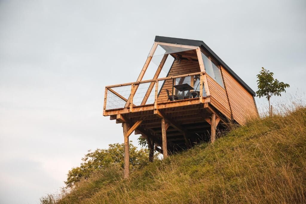 Eine Holzhütte mit Glasbalkon auf einer grünen Anhöhe.