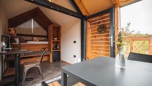 Habitación compacta y moderna con cama estilo altillo, zona de comedor con mesa y sillas, y un amplio ventanal con vistas al exterior.