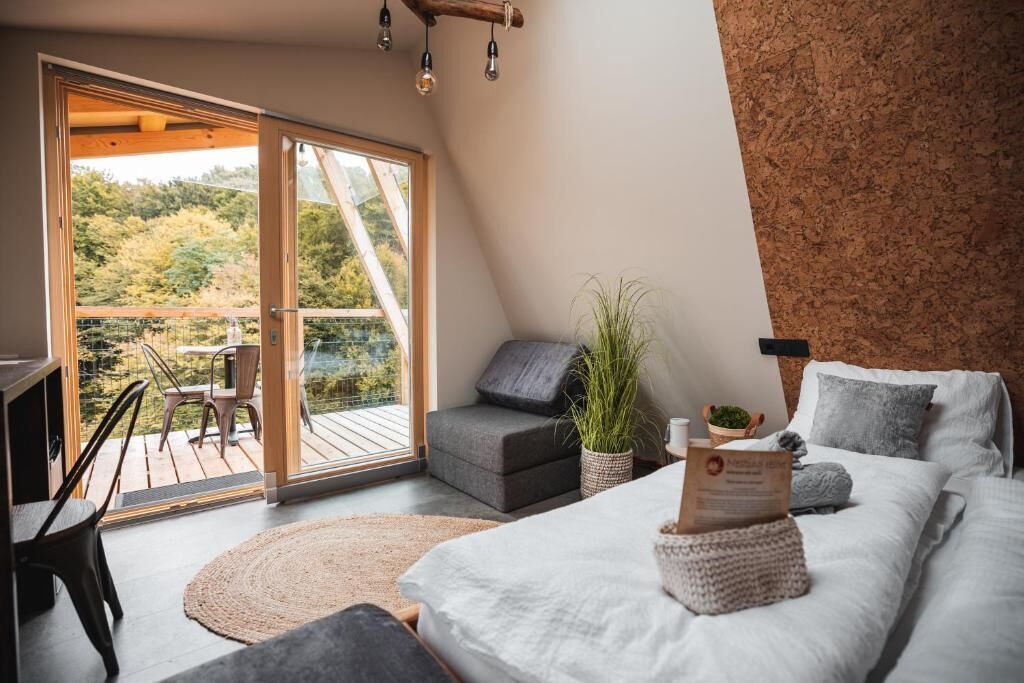 Une chambre à coucher comprenant un lit, un bureau, une chaise, un canapé et un balcon avec vue sur les arbres.