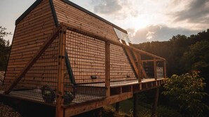 Una estructura de madera con techo triangular y balcón, rodeada de árboles.