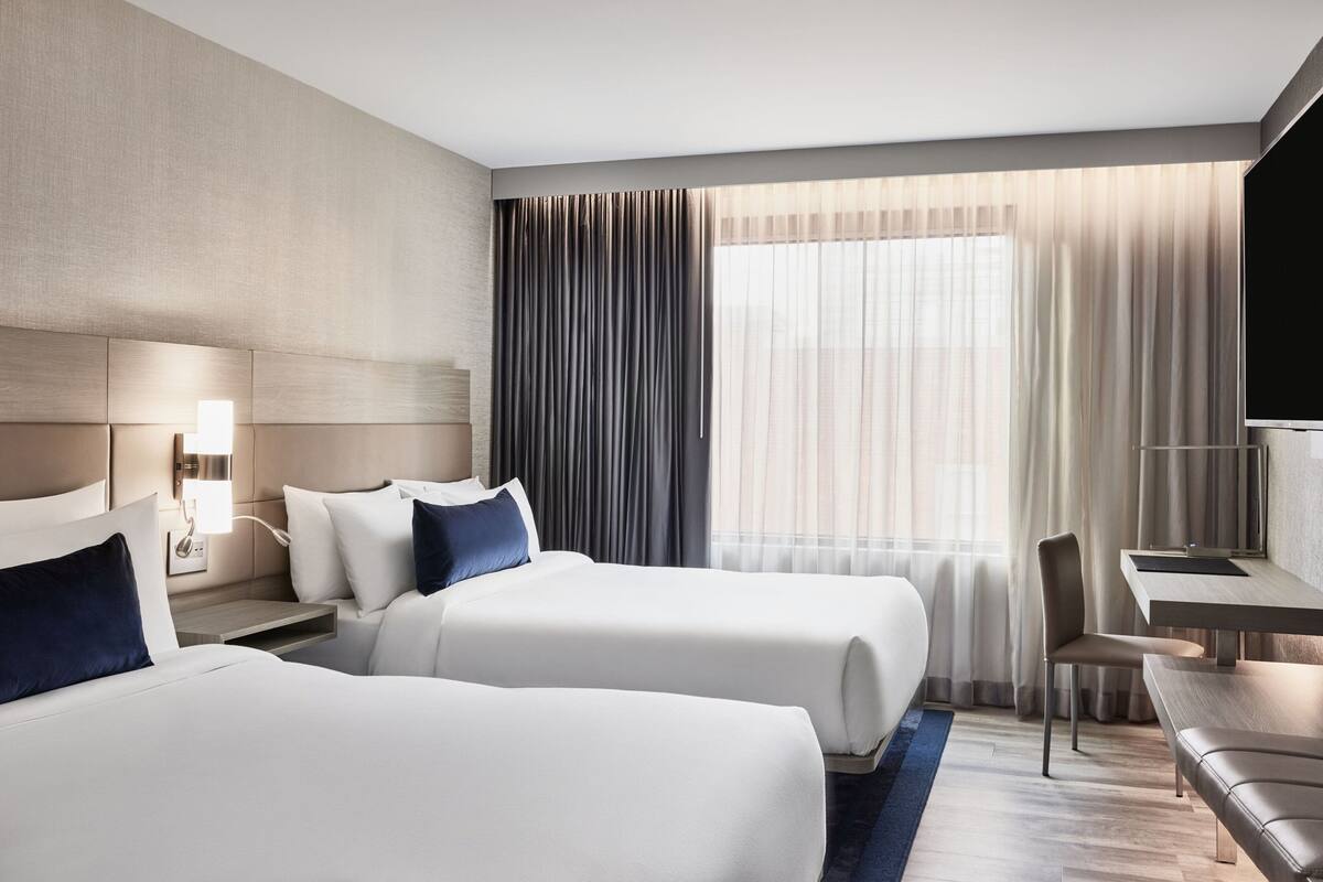 Ein Hotelzimmer mit zwei Betten, einem Schreibtisch, einem Stuhl und einem Fernseher.